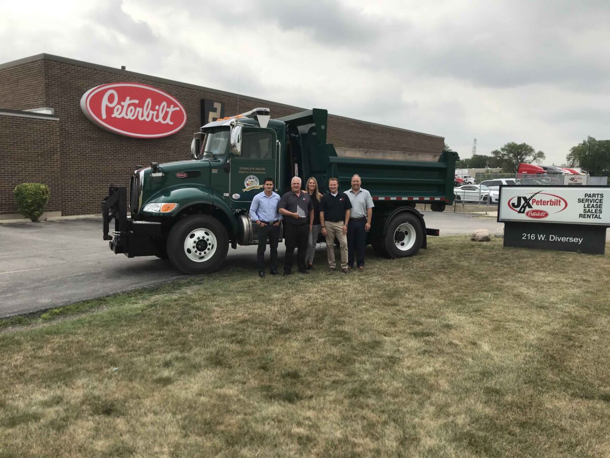 JX Employees collect sourcewell award Most Valuable Partner Award for extraordinary truck sales posing in front f peterbilt truck
