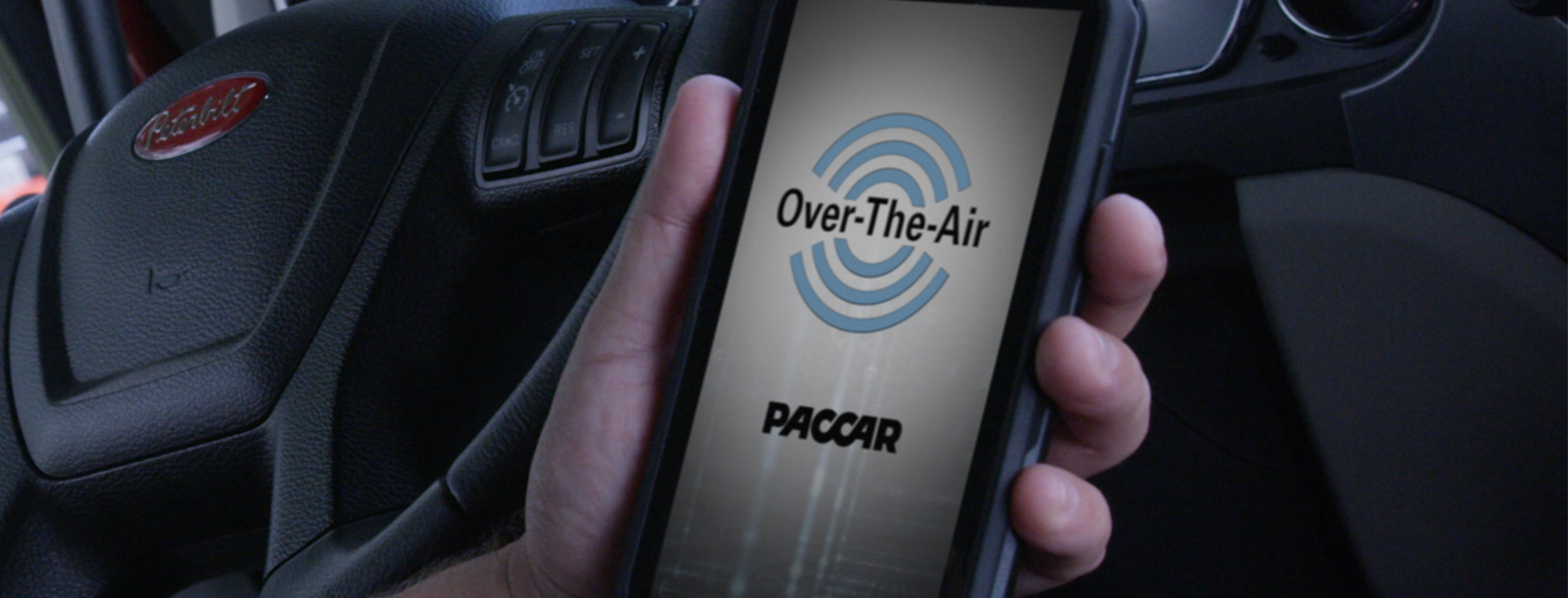 Driver holding smart phone looking at Paccar OTA software update or Over The Air app in truck